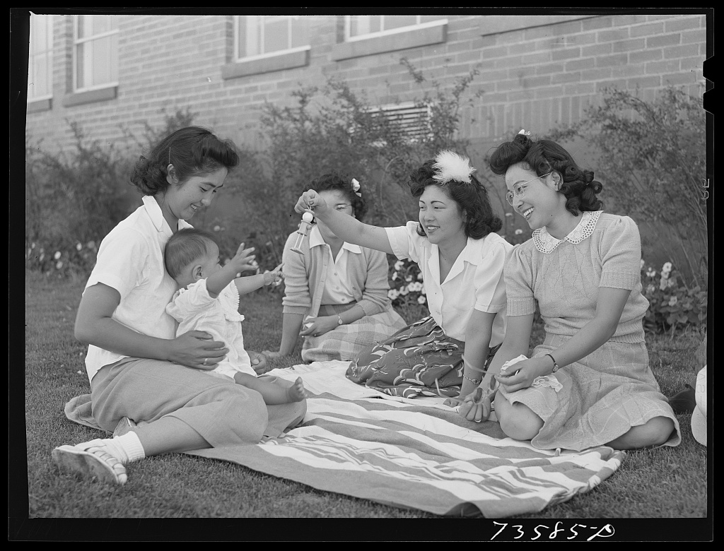 Japanese American adults and children sit and stand beside a baseball field in Nyssa, Oregon, in July 1942.